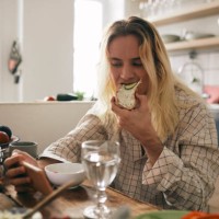 transgender person eating bread while watching mobile phone at home - food stock pictures, royalty-free photos & images