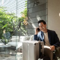 travelling asian businessman smiles at an airport lounge after receiving great news over the phone - travel stock pictures, royalty-free photos & images