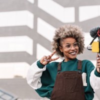 trendy african american woman influencer filming video with smartphone doing peace victory sign with hand - fashion stock pictures, royalty-free photos & images