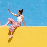 trendy woman sitting on yellow wall while taking a selfie - fashion stock pictures, royalty-free photos & images
