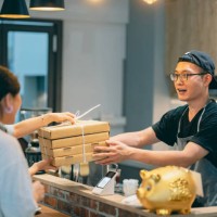 two asian customers come to pick up their take-out pizzas, and the pizza shop owner personally hands over the ordered meals to them. - junk food stock pictures, royalty-free photos & images