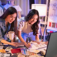 two asian female cloth designer discussion at night brainstorm new ideas,asian partners team looking at new deign sketch collection on table at home studio,.working late creative digital development agency - fashion stock pic