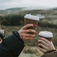 two beautiful young woman hold cardboard coffee cups and make a celebratory toast by bumping them together - junk food stock pictures, royalty-free photos & images
