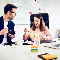two colleagues talking during lunch break in office - junk food stock pictures, royalty-free photos & images