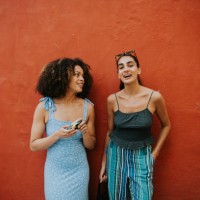 two fashionable young woman stand against a bright red wall - fashion fotografías e imágenes de stock