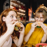 two female friends eating burger in a restaurant - food stock pictures, royalty-free photos & images