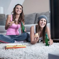 two female friends side by side on carpet at home watching television - junk food stock pictures, royalty-free photos & images