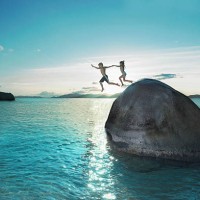 two kids holding hands jumping off rock into sea - travel stock pictures, royalty-free photos & images