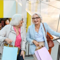 two senior women are walking up the stairs in a shopping mall while having fun shopping - fashion stock pictures, royalty-free photos & images