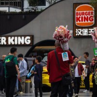 Two street vendors selling candied hawthorn walk past a Burger King restaurant during the National Day Golden Week holiday on October 5 in Chongqing,...