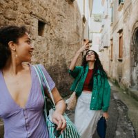 two stylish woman walk down an alleyway. one takes a photo using her mobile phone. - travel stock pictures, royalty-free photos & images