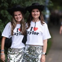 Two Taylor Swift fans are seen wearing matching outfits, consisting of black cowboy hats, white “I love Taylor” t-shirts, silver glitter mini skirts,...