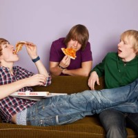 two teenage boys eating pizza while another watches enviously - junk food stock pictures, royalty-free photos & images