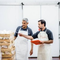 two workers taking inventory of packaged meat wooden boxes in warehouse - food stockfoto's en -beelden