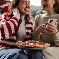 two young woman ordering pizza for a cozy night in - junk food stock pictures, royalty-free photos & images