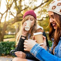 two young women drinking coffee in a park in autumn - junk food stock pictures, royalty-free photos & images