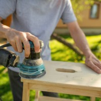 un homme âgé ponçant une chaise à l’extérieur dans la cour arrière yard par une soirée ensoleillée. rénovation de meubles anciens. concept de durabilité. - garden decoration photos et images de collection