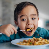una vista frontal de un niño hambriento de raza mixta comiendo arroz frito para el almuerzo con una cuchara. el fondo está borroso. - food fotografías e imágenes de stock
