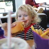 upset toddler being given burger in fast food restaurant - junk food stock pictures, royalty-free photos & images