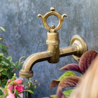vintage bronze faucet on a gray wall surrounded by plants. garden brass faucet - garden decoration stock pictures, royalty-free photos & images