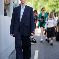 Vittoria Ceretti wears sunglasses, a blue shirt, a navy blue oversized blazer jacket, wide leg flared suit pants, sneakers, a black leather bag,...