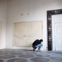 Vogue, November 15, 1966 - Artist Cy Twombly squatting to nail a large canvas on the wall in his apartment in a palazzo in Rome.