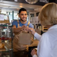 waiter giving a paper bag to a client buying pastries at a cafe - junk food stock pictures, royalty-free photos & images