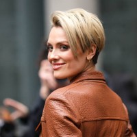 Wallis Day wears gold earrings, a camel shiny leather long coat , outside David Koma, during London Fashion Week February 2023 on February 18, 2023...