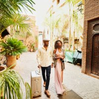wide shot of couple arriving in hotel courtyard with rolling luggage - travel stock pictures, royalty-free photos & images