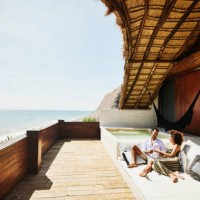 wide shot of couple relaxing on deck of luxury tropical villa overlooking ocean - travel stock pictures, royalty-free photos & images