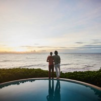 wide shot of embracing gay couple watching sunrise while standing at edge of pool at luxury tropical villa overlooking ocean - travel stock pictures, royalty-free photos & images