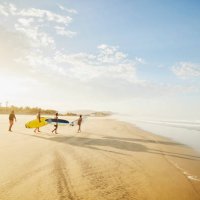 wide shot of family carrying surfboards while taking surf lesson - travel stock pictures, royalty-free photos & images