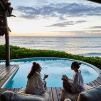 wide shot of female friends in discussion while sitting poolside at luxury suite of tropical resort at sunrise - travel stock pictures, royalty-free photos & images