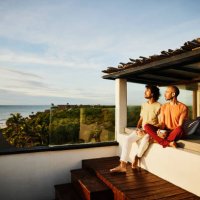 wide shot of gay couple sitting on rooftop deck of luxury tropical beachfront villa while drinking coffee and watching sunrise - travel stock pictures, royalty-free photos & images