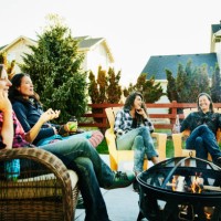 wide shot of smiling and laughing female friends hanging out by fire in backyard - garden decoration photos et images de collection