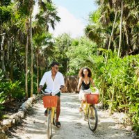 wide shot of smiling couple riding bikes to beach at tropical resort - travel stock pictures, royalty-free photos & images