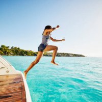 wide shot of teenage girl jumping off swim step of yacht into ocean - travel stock-fotos und bilder