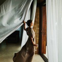 wide shot of woman standing by door of luxury hotel suite looking out at view with curtains blowing in wind - fashion stock pictures, royalty-free photos & images