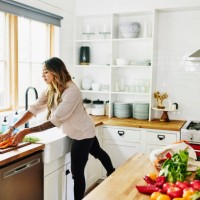 wide shot of woman washing fresh produce in kitchen sink after grocery shopping - fashion stock pictures, royalty-free photos & images