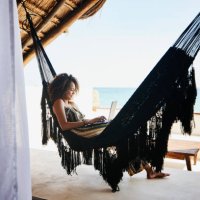 wide shot of woman working on laptop while relaxing in hammock on deck of luxury tropical villa overlooking ocean - travel stock pictures, royalty-free photos & images