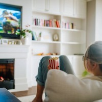 wireless tv technology and 3d. rearview of woman eating popcorn and watching tv at home - junk food stock pictures, royalty-free photos & images