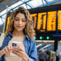 woman at the train station using her phone while checking the departure board - travel stock pictures, royalty-free photos & images