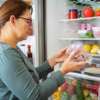 woman by the fridge reading label of refrigerated food package - food stock pictures, royalty-free photos & images