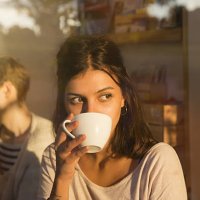 woman drinking coffee in urban cafe while looking outside, sunny reflections in window. - coffee stock pictures, royalty-free photos & images