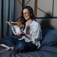 woman eating pasta and watching movie at bed at night - junk food stock pictures, royalty-free photos & images