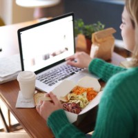woman eating takeaway food while working on her laptop - junk food stock pictures, royalty-free photos & images