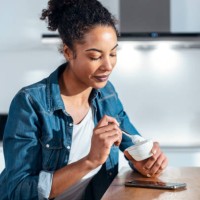 woman eating yogurt sitting in kitchen at home - food stock pictures, royalty-free photos & images