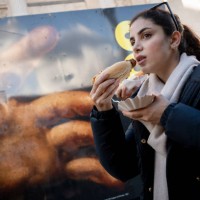 Woman eats a sausage while walking past a large detail reproduction of Caravaggio's 'The Supper of Emmaus' outside the National Gallery that is in...