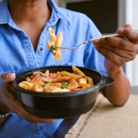 woman eats takeout pasta and chicken dish - junk food stock pictures, royalty-free photos & images