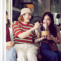 woman feeding noodles to female friend - junk food stock pictures, royalty-free photos & images
